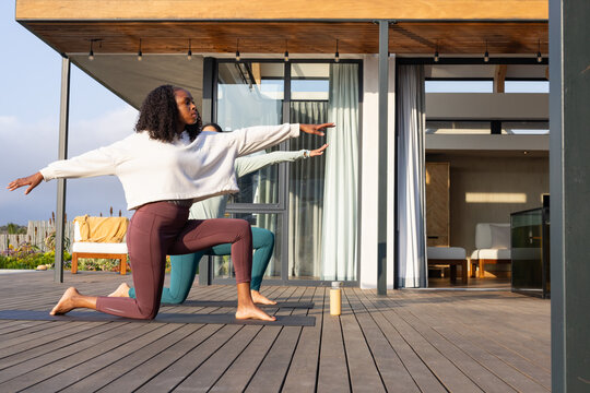 Diverse female partners practicing yoga on wood deck in maroon leggings using mats and water bottle