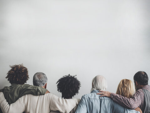 Back view of a diverse group of people standing together with hands and arms visible, symbolizing unity, inclusion, and emotional connection. No faces shown. Minimal background.
