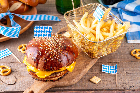 Oktoberfest Burger menu with french fries, pretzels, beer bottles. Tasty cheese hamburger in pretzel bun, with french fries, bavarian beer snacks, with checkered tablecloth and Oktoberfest decor