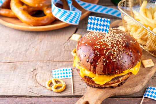 Oktoberfest Burger menu with french fries, pretzels, beer bottles. Tasty cheese hamburger in pretzel bun, with french fries, bavarian beer snacks, with checkered tablecloth and Oktoberfest decor
