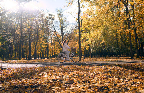 Woman cycling through a sunlit autumn park.
