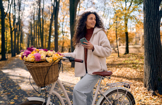 Woman cycling with flowers in an autumn park.