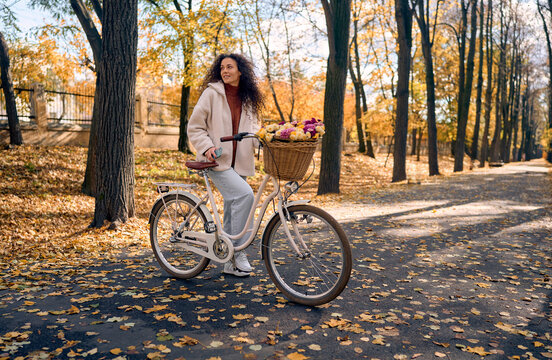 Woman with flower basket cycling through an autumn park.