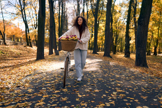 Woman with flower basket bicycle in autumn park.