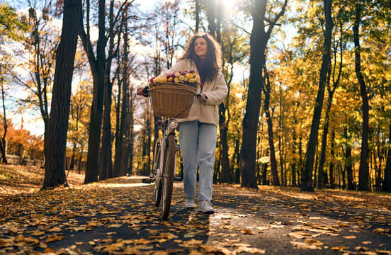 Woman walking a bicycle through a sunny autumn park.
