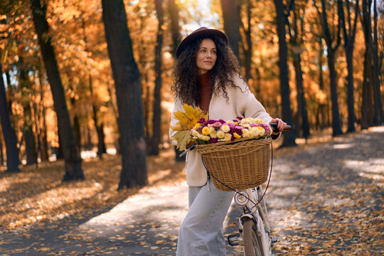 Woman cycling through an autumn park with flowers.