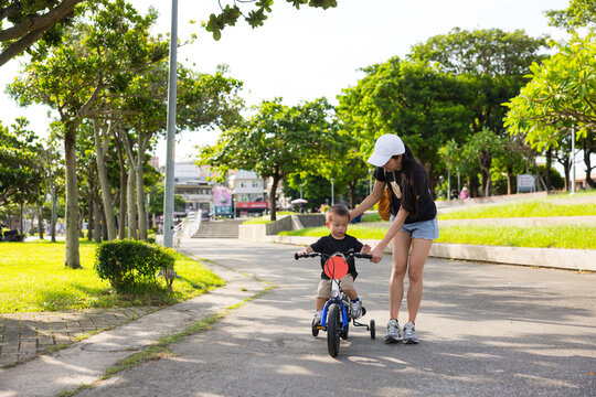 Mother helping young child ride bicycle on path