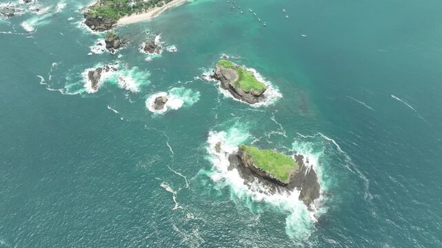 Aerial view of Papuma Beach with rocky outcrops and turquoise waves crashing against the shore in Jember, East Java, Indonesia.