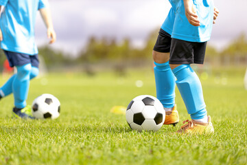 Fototapeta premium Close-Up of Junior Soccer Players in Light Blue Kits Dribbling Soccer Balls - Youth Football Training Drill and Ball Control Practice on Grass