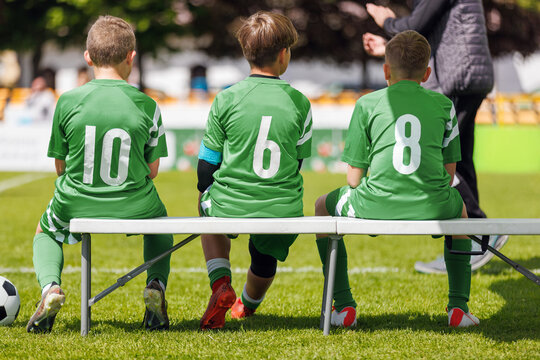 Junior Soccer Substitutes in Green Jerseys 10, 6, and 8 Sitting on Sideline Bench