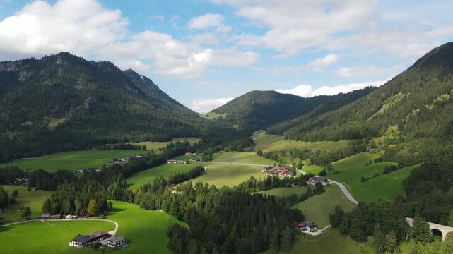 Aerial drone view of the idyllic Bavarian Alps near Ramsau bei Berchtesgaden, Germany, featuring lush green alpine meadows, narrow country roads and majestic mountain scenery. Peaceful rural footage