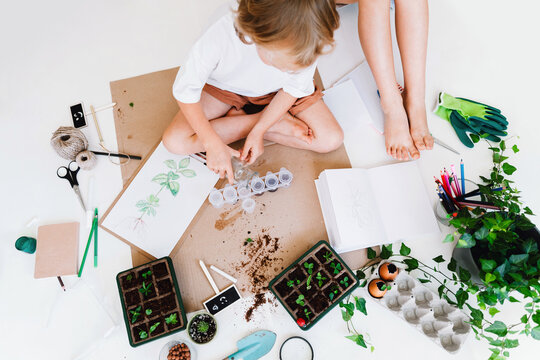 A little girl sits on the floor indoors and carefully pours water into small plastic test tubes. Creative home laboratory concept for ecology and futurism experiments.