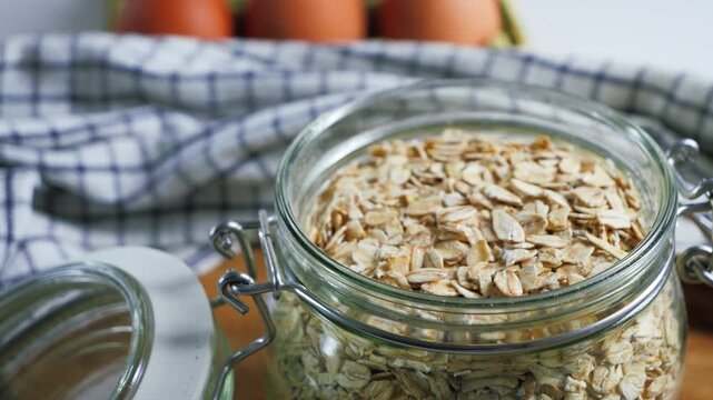 Close-up of dry oat flakes in a glass jar on a table, a nutritious whole grain ingredient for a healthy breakfast.