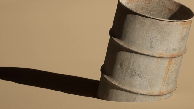 A metal container stands partially buried in the sand. The sun casts a strong shadow across the smooth surface. The scene shows a simple display of objects in a sandy area.