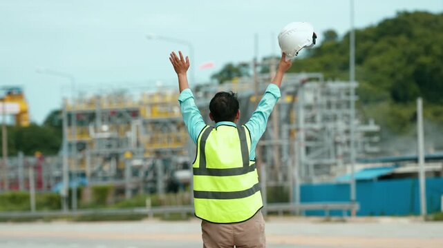 Construction worker hard hat and reflective vest raising helmet active building site, celebrating workplace safety, construction progress, urban development, and achievement near industrial