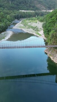 Aerial view of the suspension bridge over the Vara river surrounded by lush green forest in Province of La Spezia, Liguria, Italy.