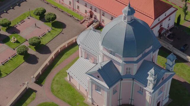Aerial view of the Church of the Holy Trinity with its distinctive dome and pink walls surrounded by green lawns and paved paths in Liskiava, Alytus County, Lithuania.