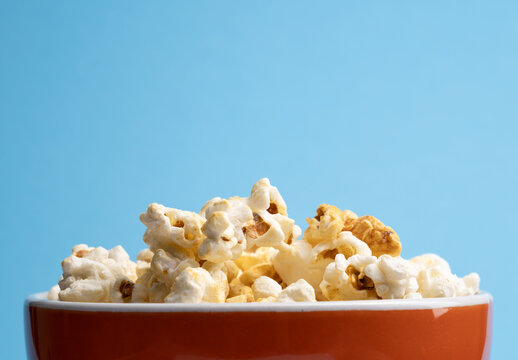 Fresh organic popcorn in an orange bowl on a blue background