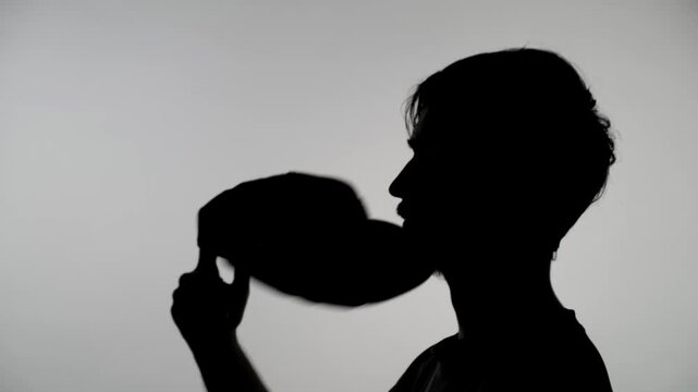 A close-up of an anonymous silhouette of a man twirling his cap, putting it on, and taking it off