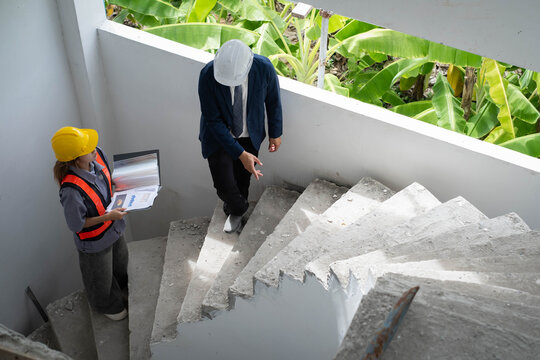 Construction engineer inspecting an unfinished concrete staircase with a site supervisor, reviewing structural safety, project progress, quality control, building inspection, construction management.