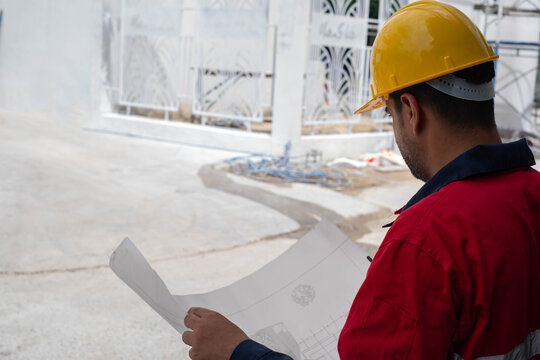 Construction engineer reviewing architectural blueprint at a residential construction site, planning project execution, verifying site conditions, and ensuring quality, safety, and workflow accuracy.