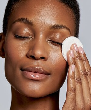 A young woman cleanses her face with a cotton pad and toner, creating a fresh and wellness-focused visual suitable for skincare or beauty branding.