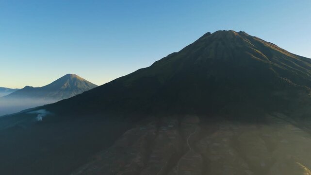 Aerial view of the majestic Mount Sumbing and Mount Sindoro volcanoes at sunrise with terraced agricultural slopes in Kaliangkrik, Central Java, Indonesia.
