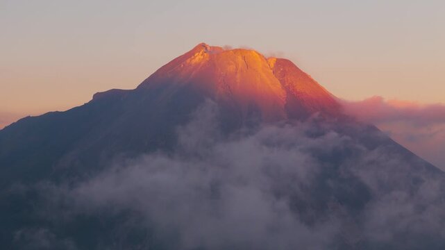 Aerial view of Mount Merapi illuminated by golden hour light with clouds surrounding the volcanic peak in Dukun, Central Java, Indonesia.