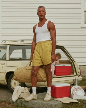 Man loading a tan canvas duffel and red cooler into a car boot, featuring a calm early-morning mood with copy space for travel campaigns