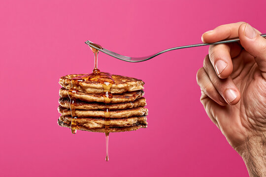 Stack of homemade pancakes being drizzled with sweet syrup from metal fork