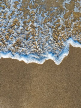 Top view of white sea foam wave on wet sandy beach with copy space.