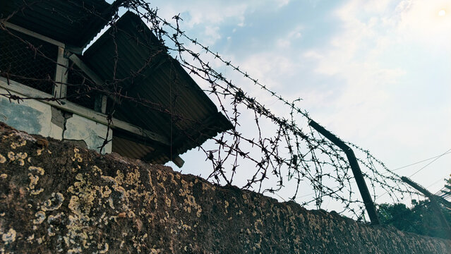 Rusty barbed wire fence on a weathered concrete wall against a bright sky