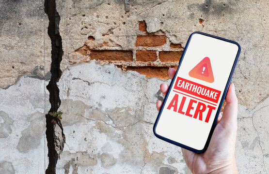 Earthquake alert on smartphone over crack wall background, emergency alert, Natural Disaster warning