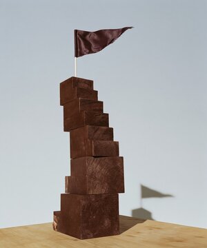 Wooden block staircase with a small brown pennant flag on top, featuring raw timber textures and a bright background for business growth copy space