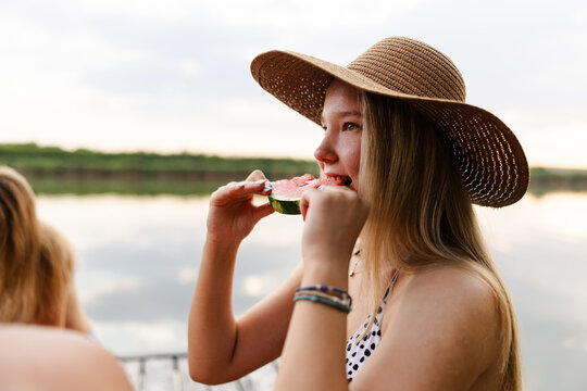 Teen Girl Enjoys Watermelon by the River During a Summer Afternoon With Friends
