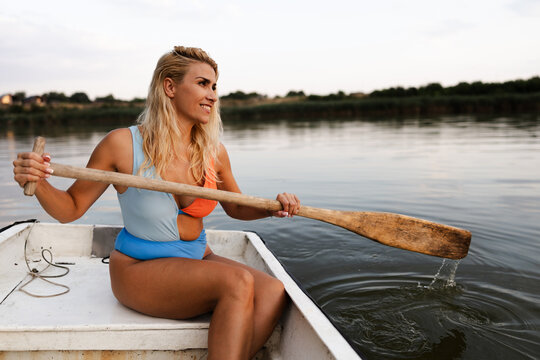 Woman Paddles a Small Boat on a River During Summer While Enjoying the Warm Weather and View of the Surrounding Landscape