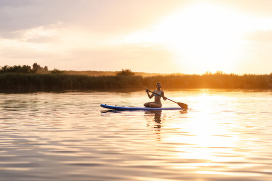 Teen Girl Paddleboarding on a Summer Evening River During Sunset