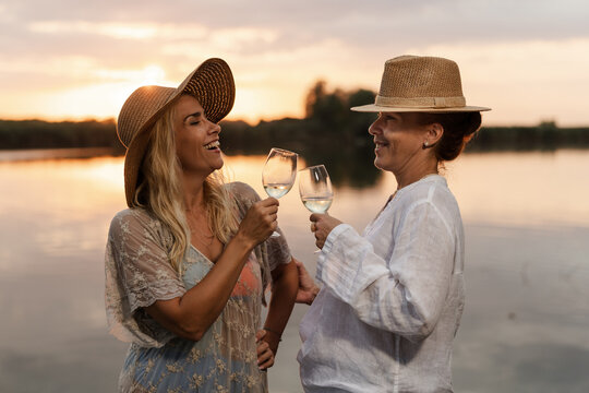 Two Women Celebrate Summer by the River During Sunset While Holding Glasses of Wine