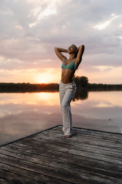 Teen Girl Enjoys Summer Evening by the River With Sunset in the Background and Warm Colors in the Sky