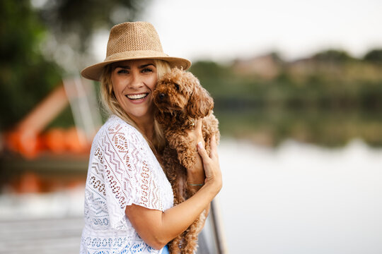 Woman Smiles While Holding a Dog by a River During Summer