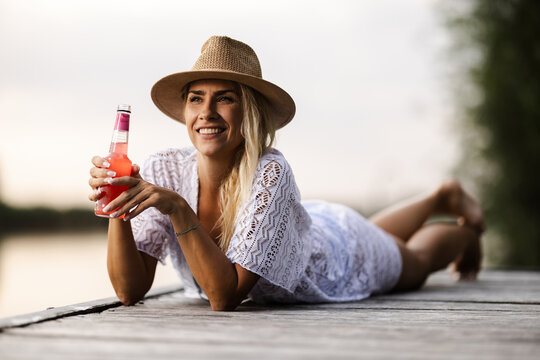 Woman Enjoys Drink by the River on a Summer Day While Lying on a Dock