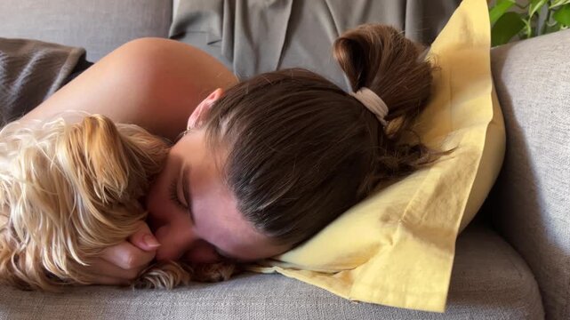 Calm young woman and her cute yorkshire terrier dog sleeping together on a cozy couch at home. Real horizontal footage