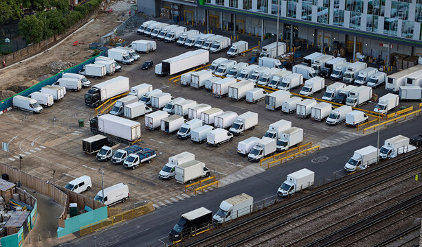 Logistics warehouse yard with delivery trucks and commercial vehicles for distribution operations. Fleet surrounding a modern loading facility beside railway tracks, freight transport, supply chain 