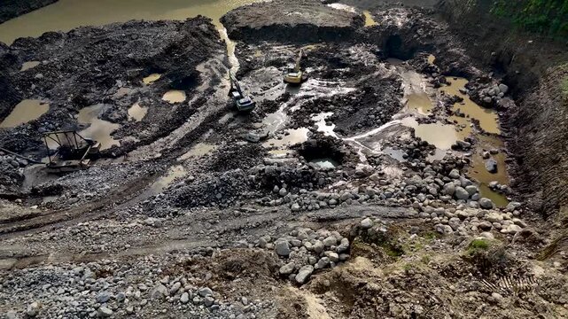 Aerial view of excavators working at the Cimangkok Sand Mining Site, featuring muddy terrain, rocky ground, and water pools in Sukabumi, West Java, Indonesia.
