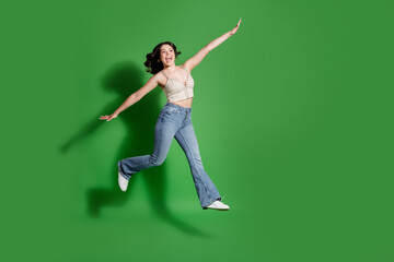 Joyful woman jumping on a green background in casual jeans and crop top conveying energetic...