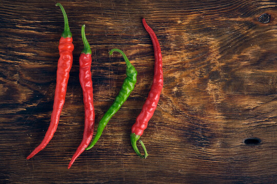 Fresh red and green hot chili peppers arranged on dark rustic wooden cutting board background.