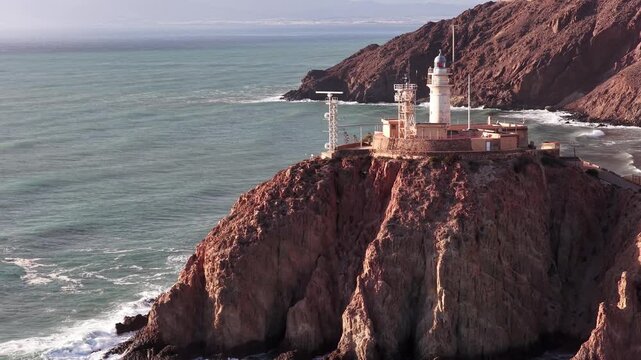 Aerial view of Faro de Cabo de Gata lighthouse perched on rugged cliffs overlooking the Mediterranean Sea in San Jose, Andalucia, Spain.