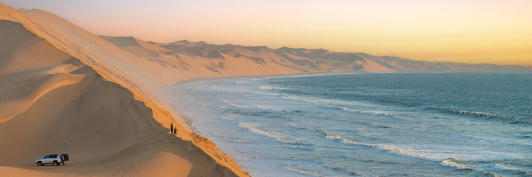 Tourists in the sand dunes and ocean view in Sandwich Harbour, Namib Naukluft Natural Park panoramic landscape in Namibia, Africa web banner