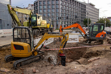 Multiple excavators at large urban construction site with modern apartment buildings and city street in background © KATSIARYNA