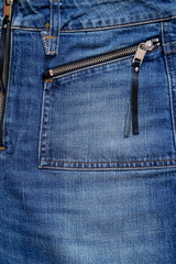 Close-up distressed blue denim jeans featuring a zippered front pocket, metal zipper, black leather pull tab, rivet, orange stitching, and texture. © Tanya